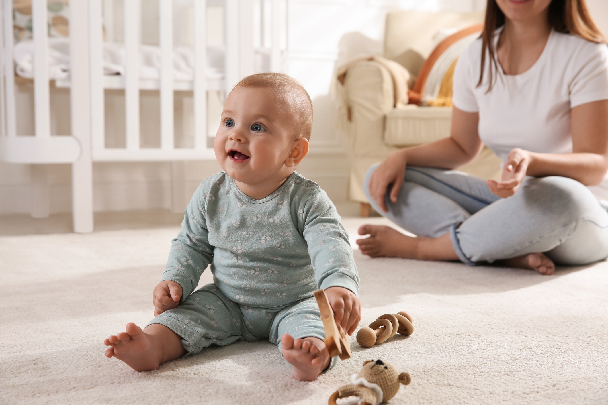 Cute baby girl playing with wooden toys and mother on floor at home when do babies sit independently