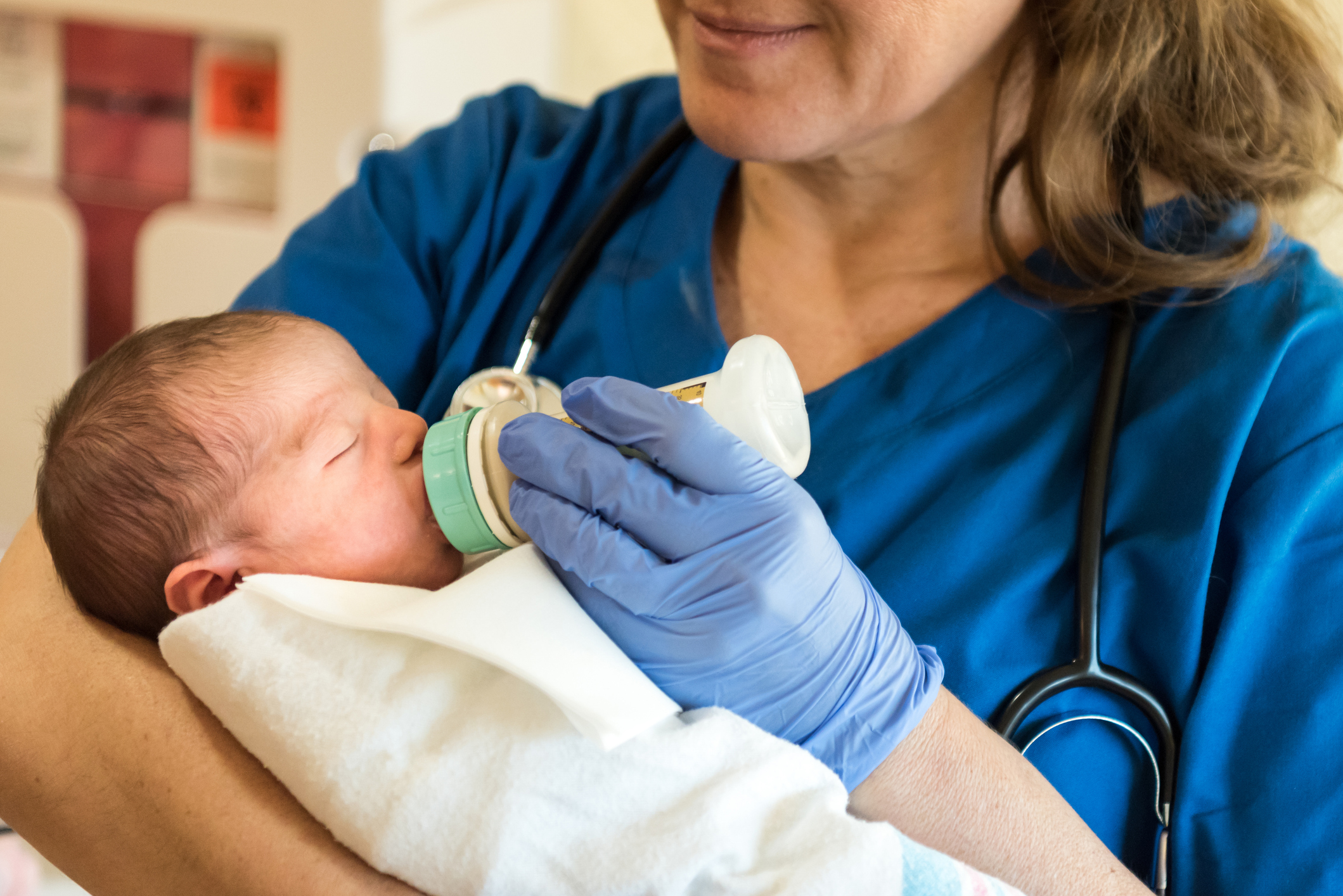 Caucasian female mature nurse feeding a newborn baby