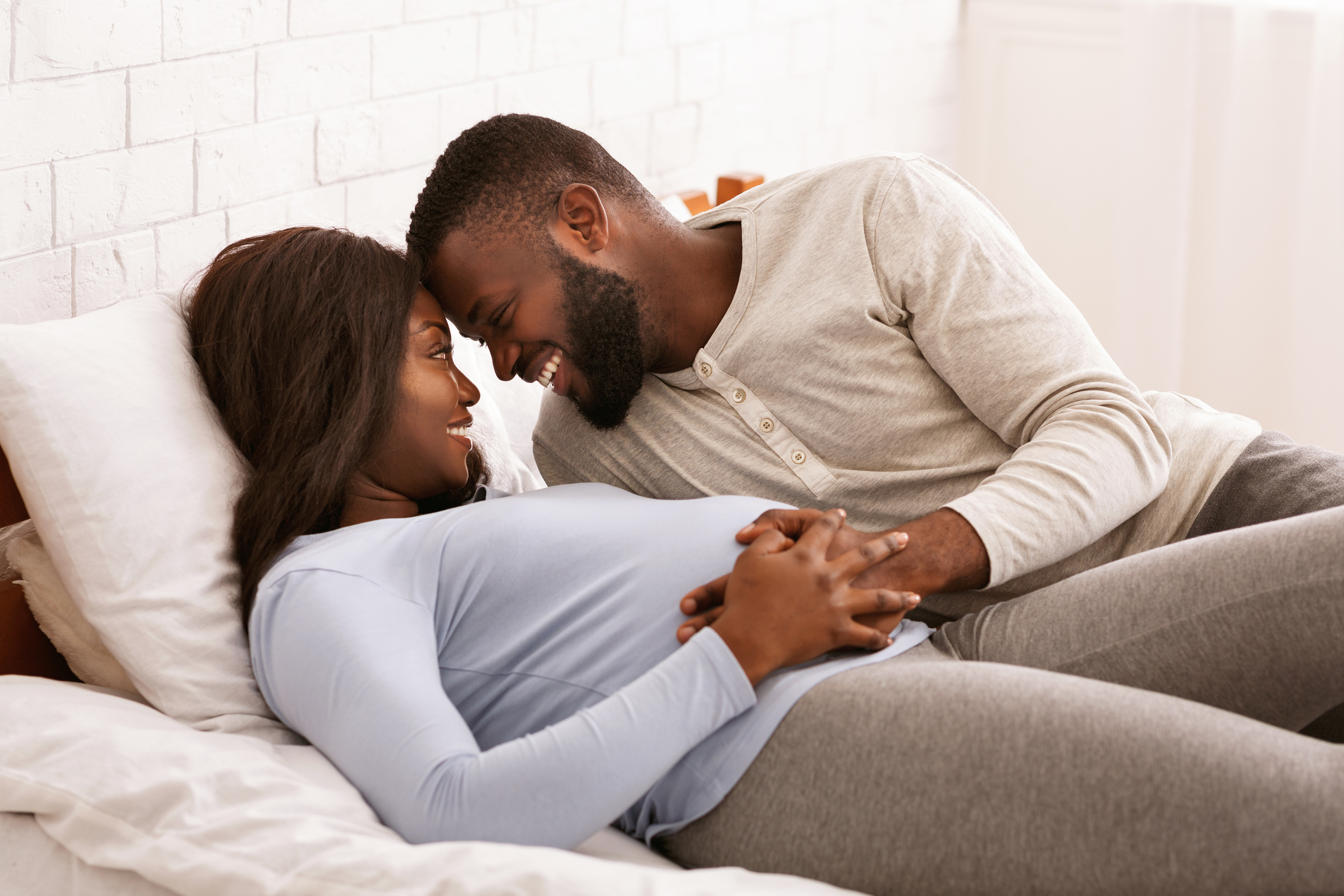 Pregnant black couple in love cuddling in bed at home, love and passionate concept