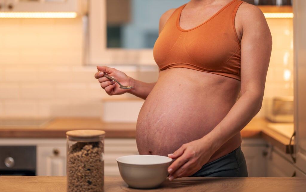 A beautiful mid adult pregnant woman in sports outfit preparing a bowl of oatmeal for breakfast.