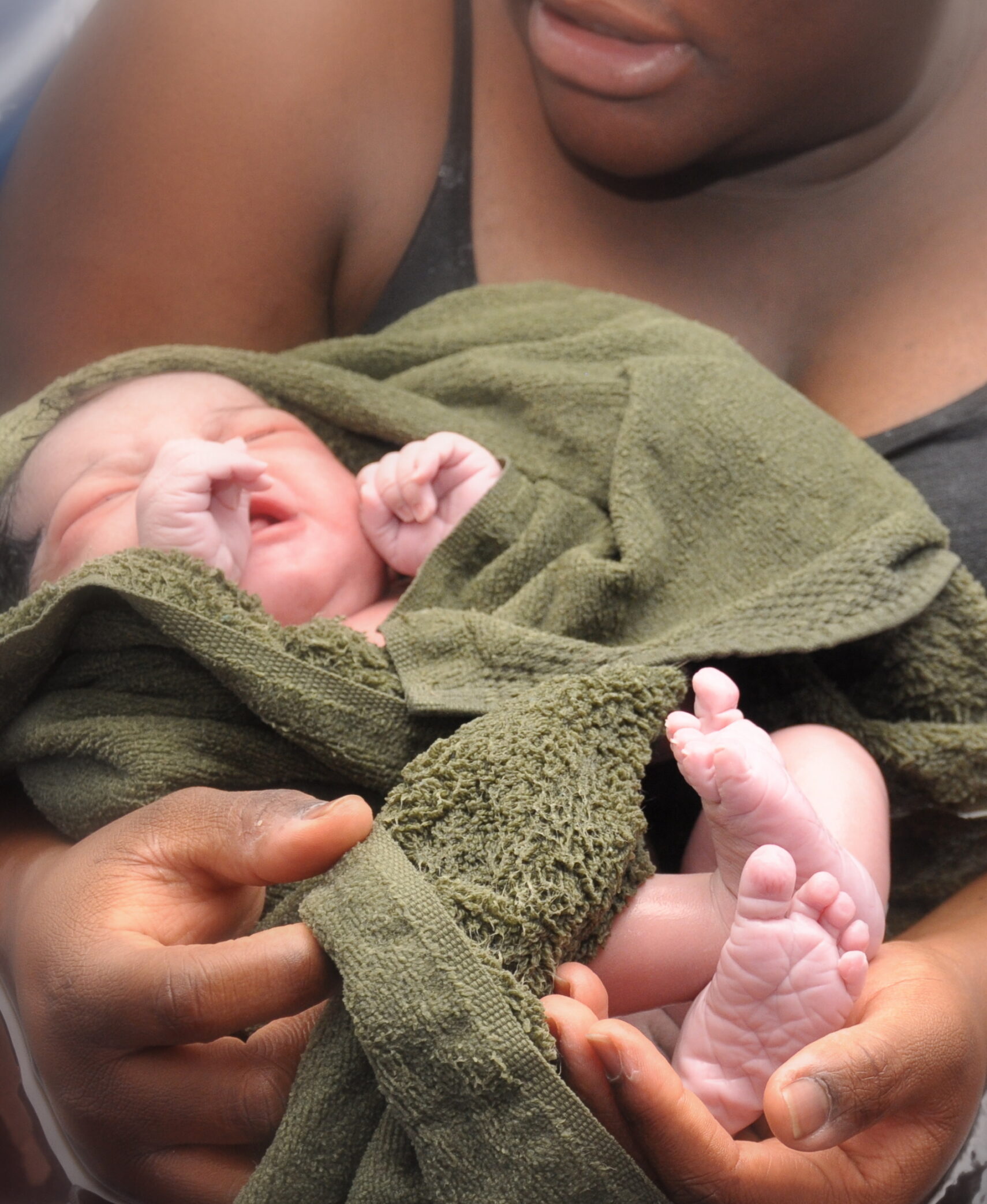 mother holding newly born daughter, her tiny feet in mommy's hand, home birth