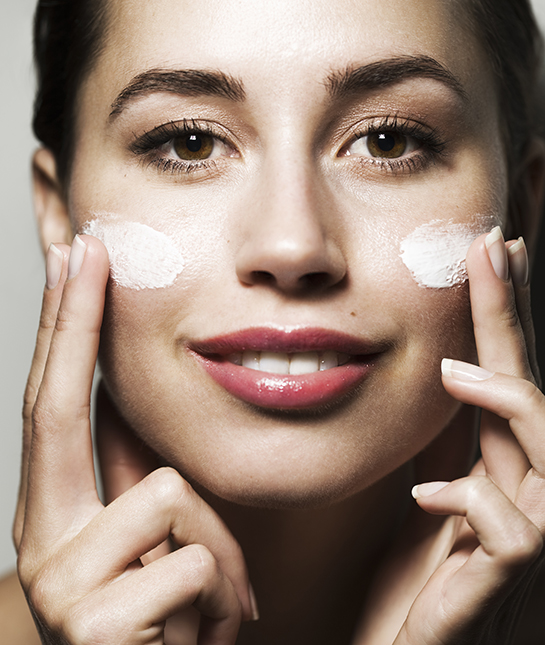 Young woman putting cream on face, smiling