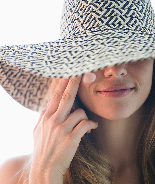 USA, New Jersey, Jersey City, Portrait of woman in straw hat applying moisturizer