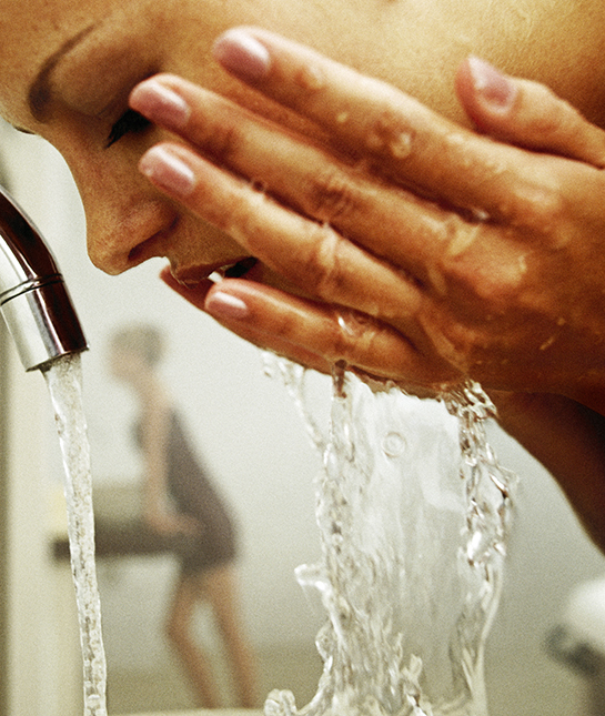Young woman splashing water on face, close-up, profile