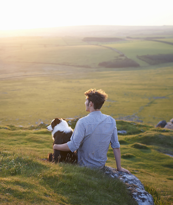 Man sitting with dog at sunset.