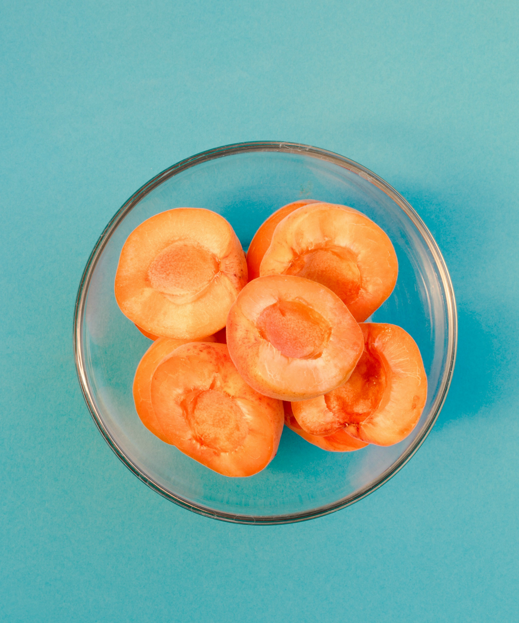 Sliced apricots in bowl on blue background