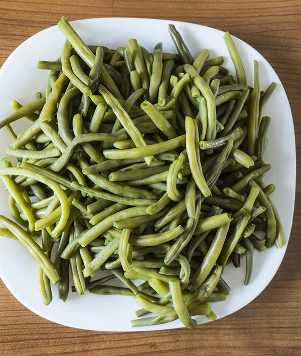 White plate of green beans boiled on a wooden table. Spain