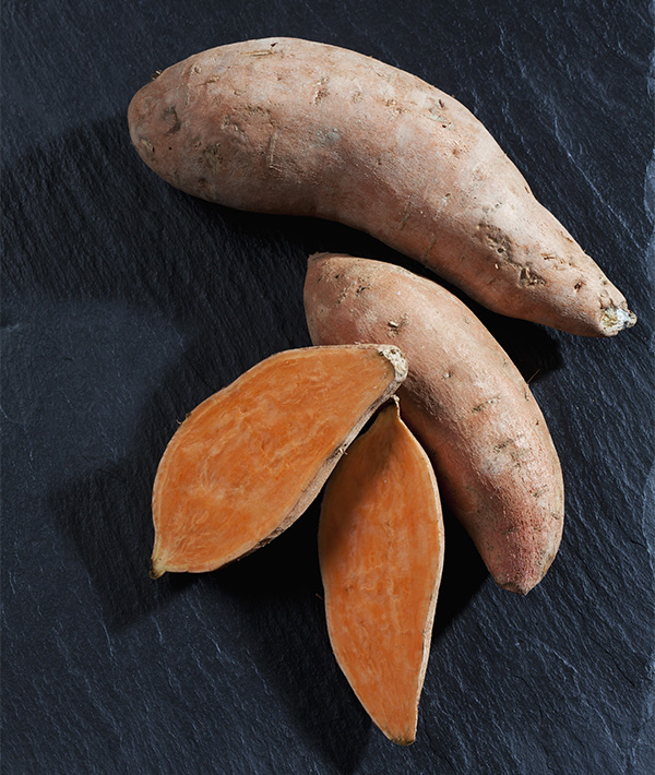 Whole and sliced sweet potatoes on slate