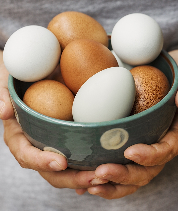 A woman holding bowl with fresh brown and white eggs.