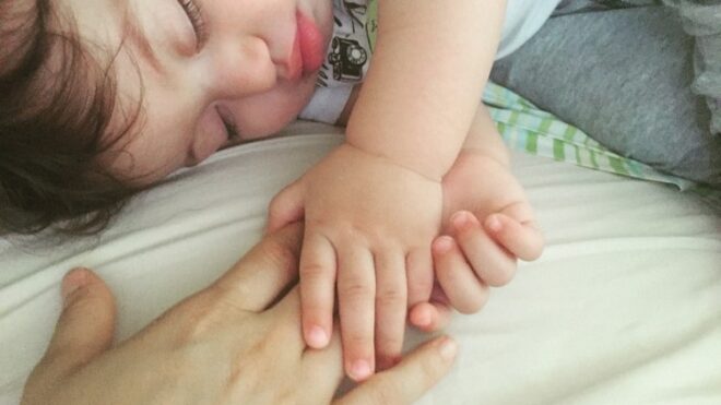 baby-holding-moms-hand-bed