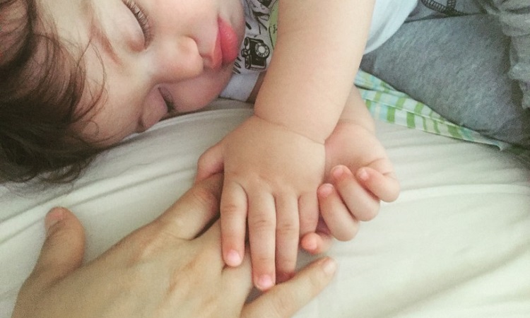 baby-holding-moms-hand-bed