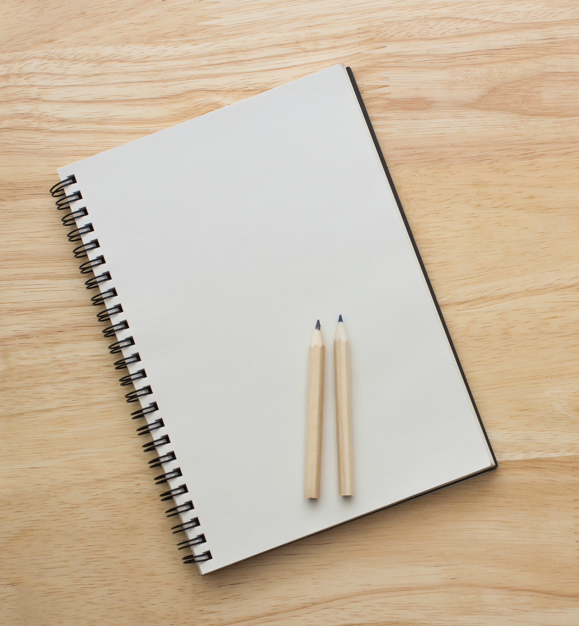 Two pencils put on notebook and put left side wooden table desk background