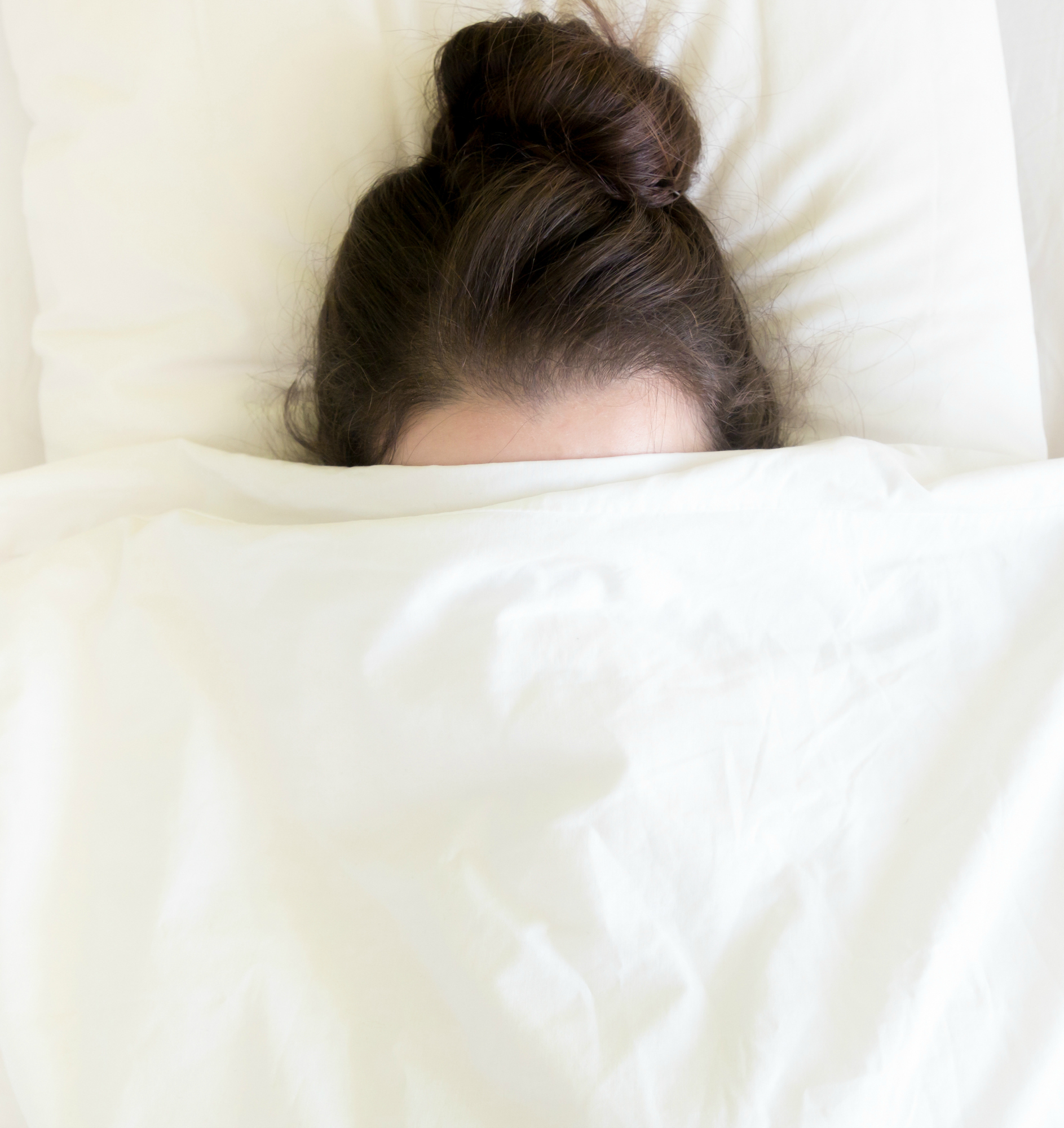 Attractive brunette young woman under blanket in the white bed at morning time