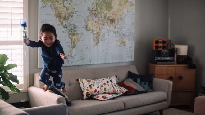 a-young-boy-jumping-off-a-couch-into-a-chair-in-a-living-room_t20_zv7e4n