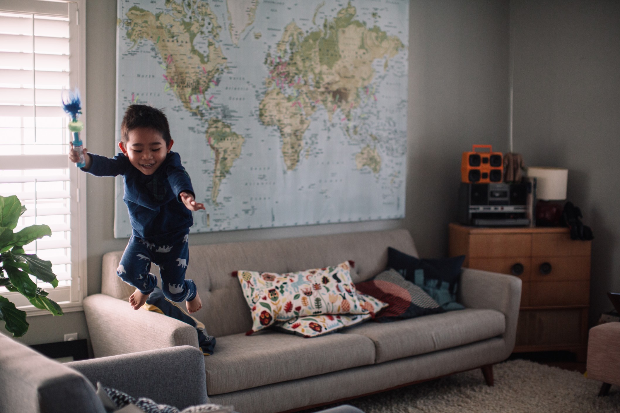 a-young-boy-jumping-off-a-couch-into-a-chair-in-a-living-room_t20_zv7e4n