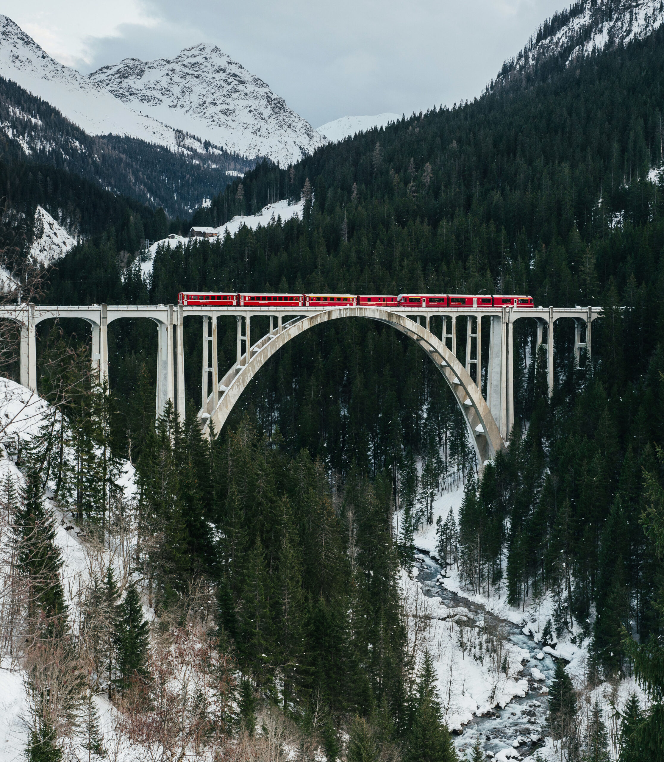The sightseeing train bernina express of Rhaetian Railway running on the Viaduct with view of colorful trees on a sunny autumn day, Canton of Grisons, Switzerland