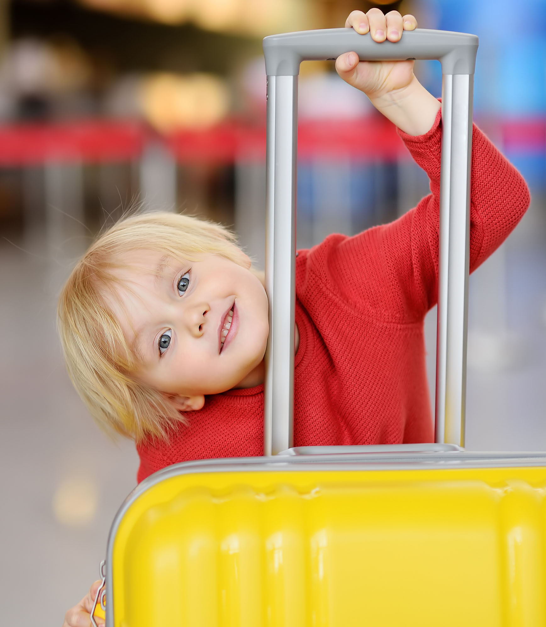 Cute happy little boy with big yellow suitcase at international airport before flight