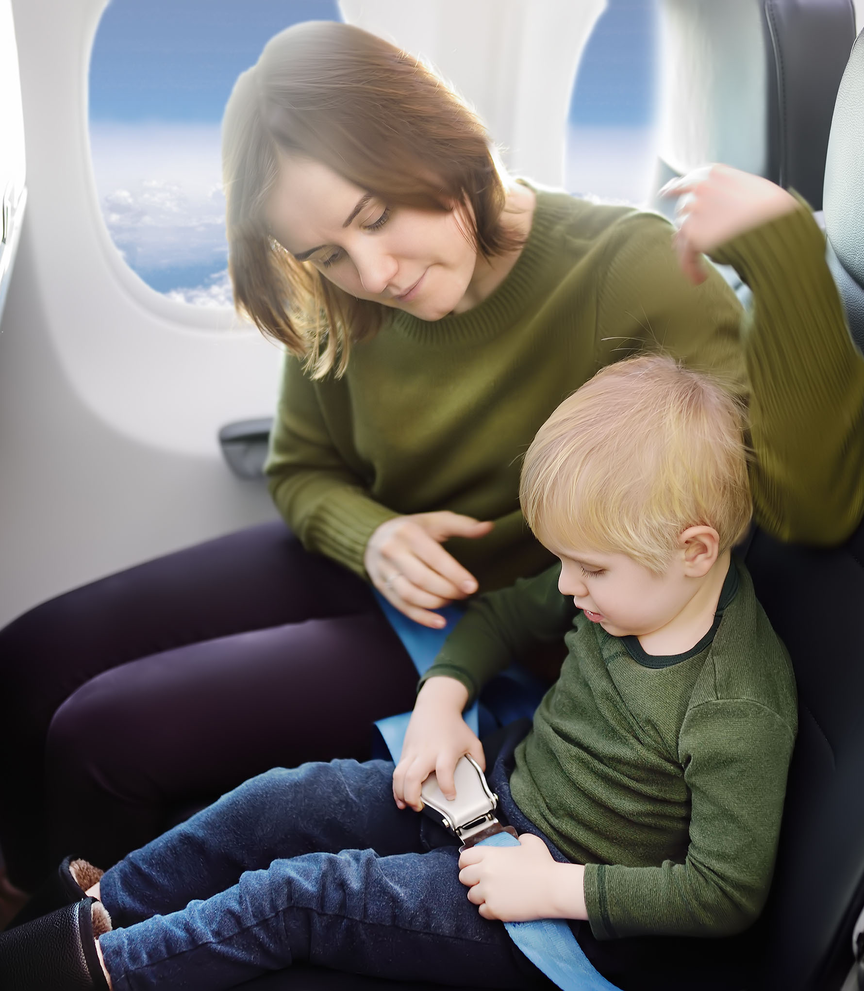 Young mother helping her little son with safety belt during traveling by an airplane