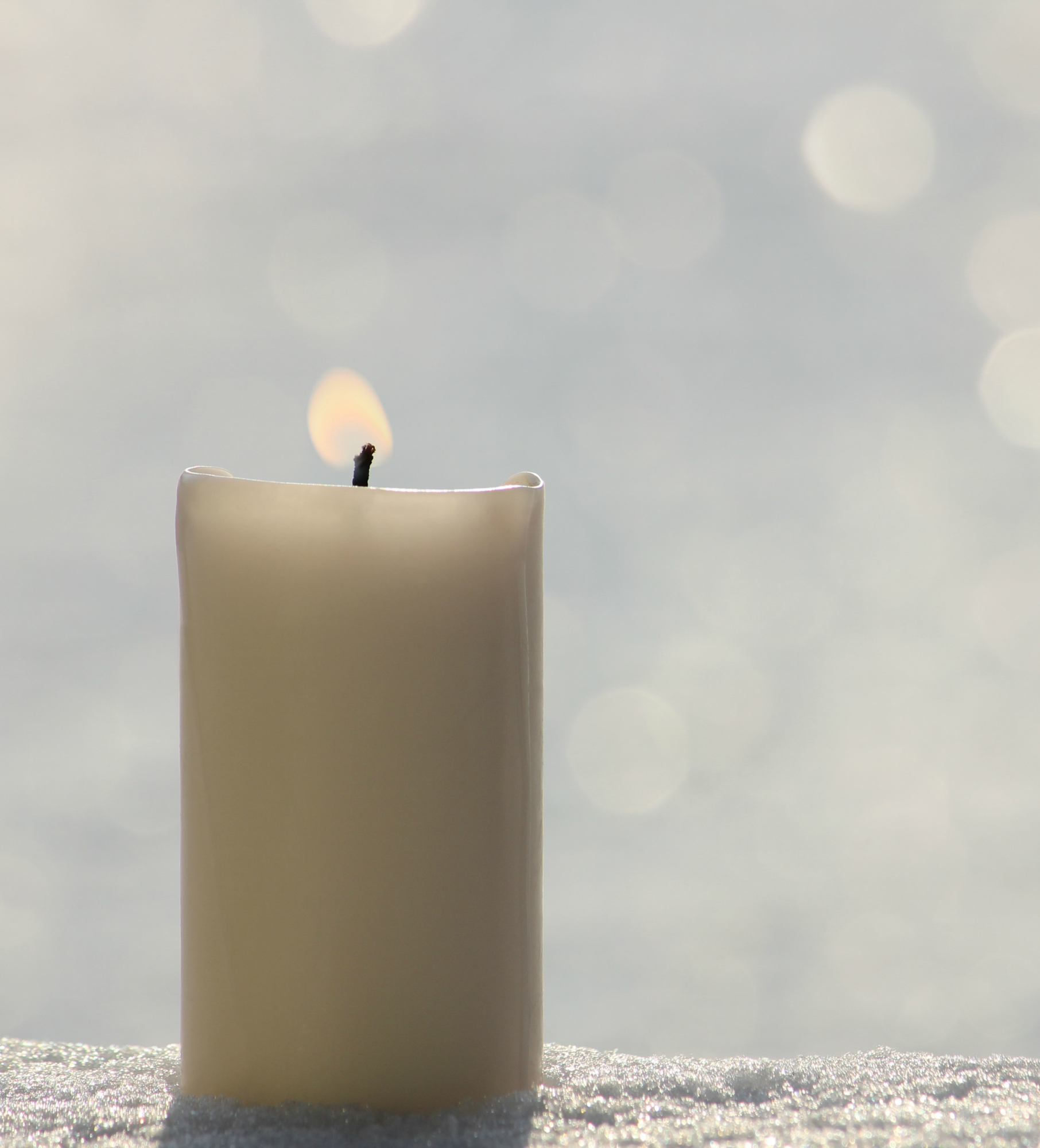 White candle on white snow background.
