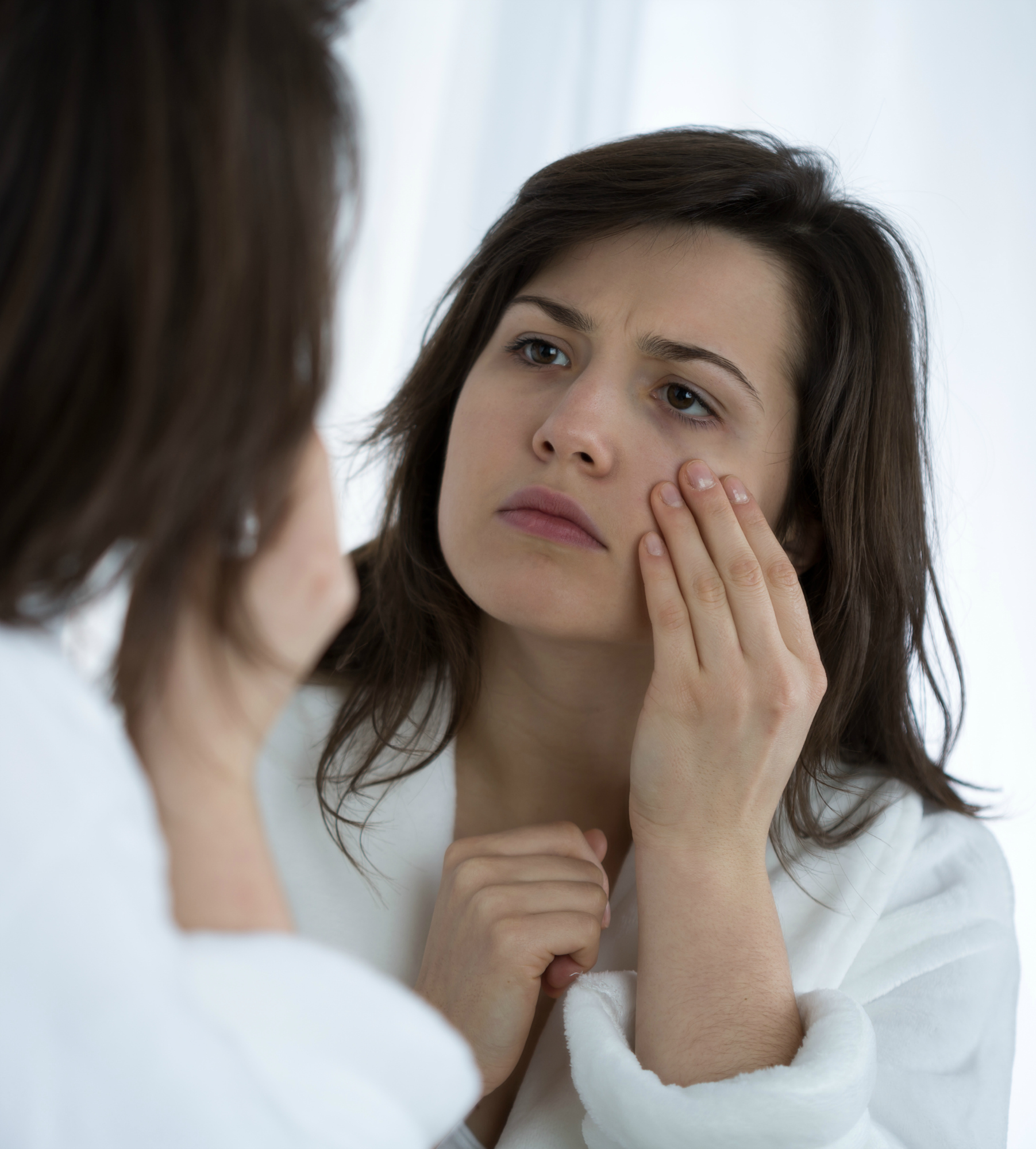 Young sad woman looking in the mirror at her wrinkles