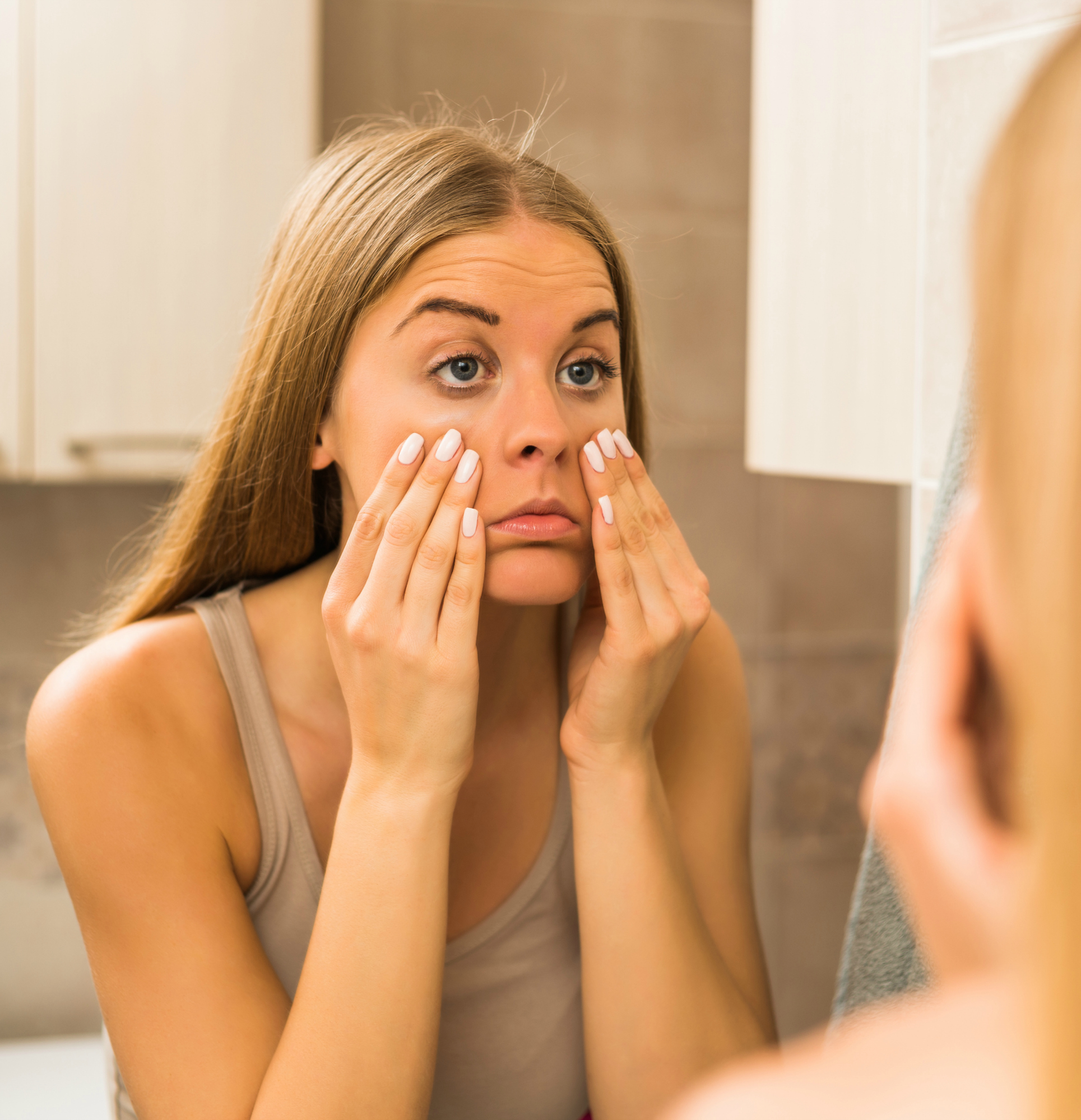 Tired woman looking her eye bags in the bathroom.