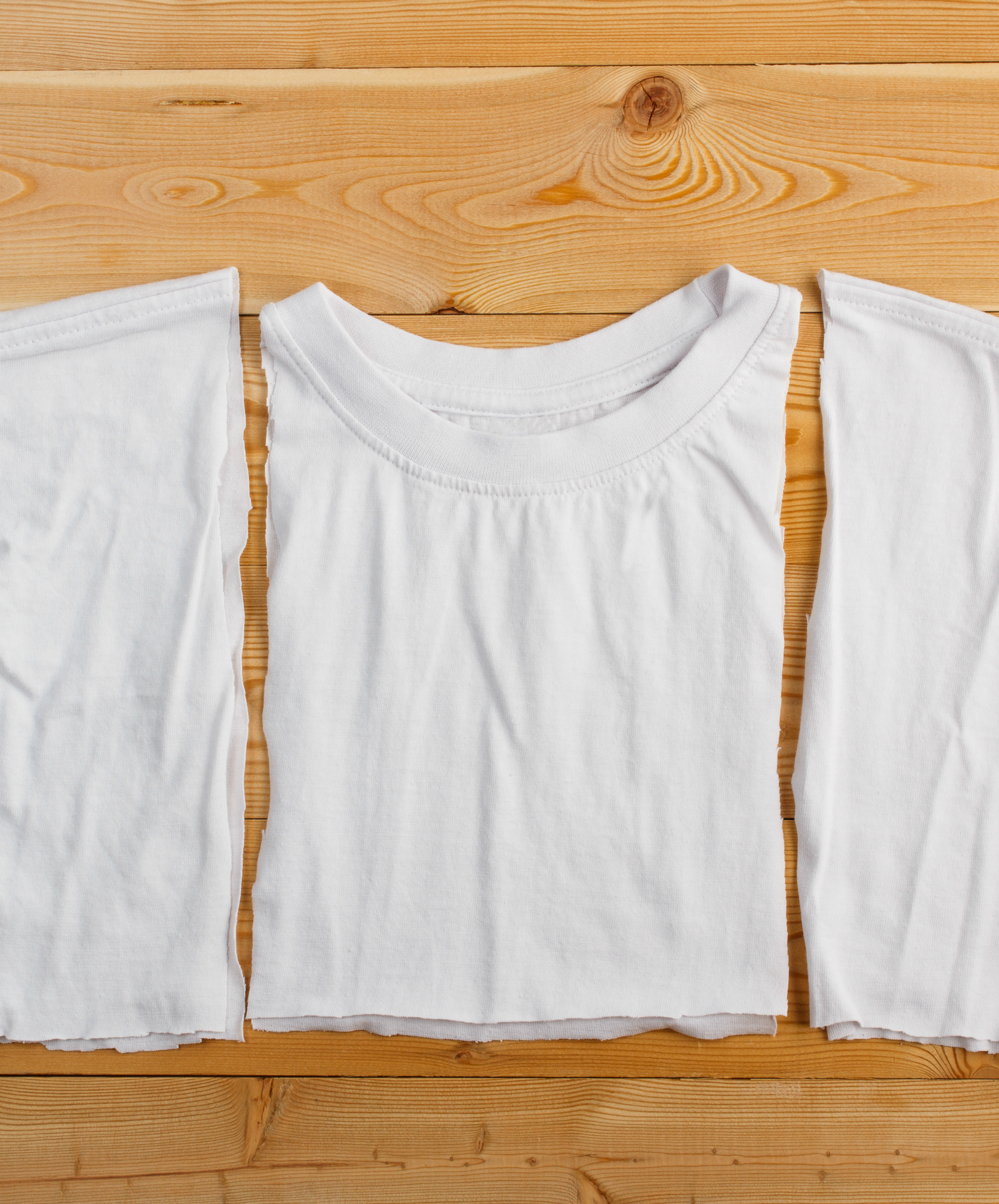 Cut white t-shirt on wooden background. Dress-making concept