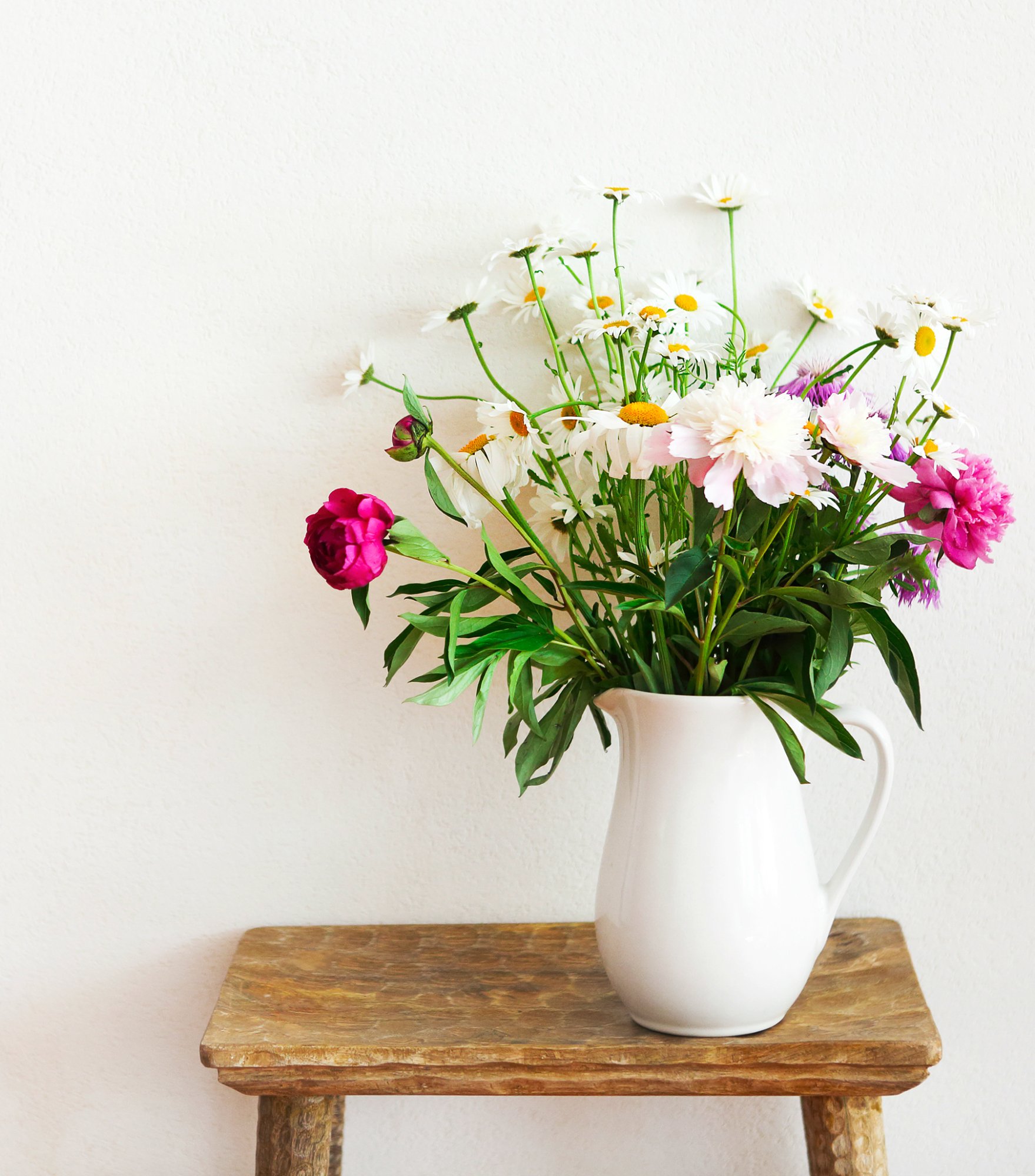 Still life with flower bouquet in white vase on wooden rustic chair