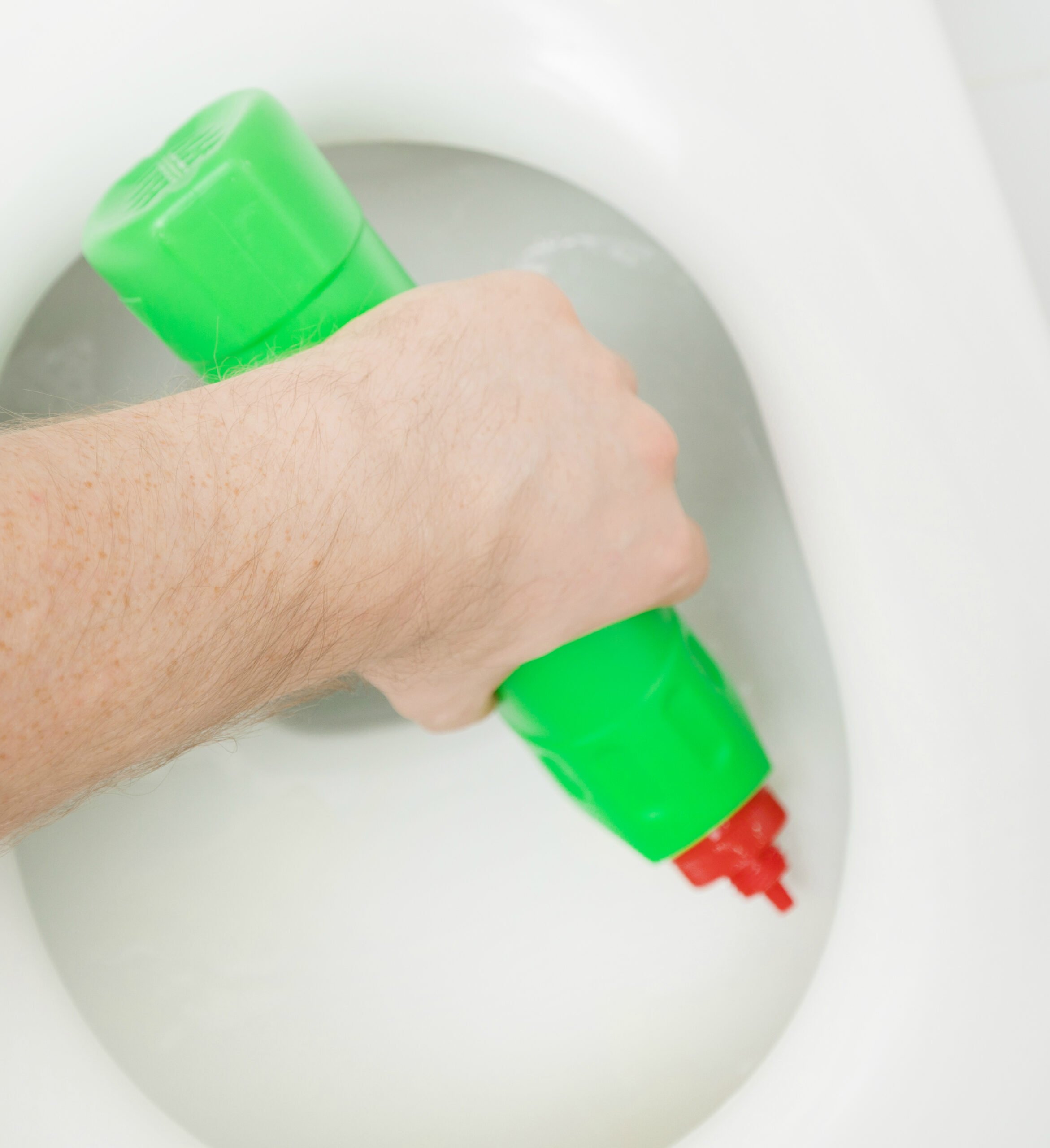 Male hand cleaning toilet bowl at water closet.