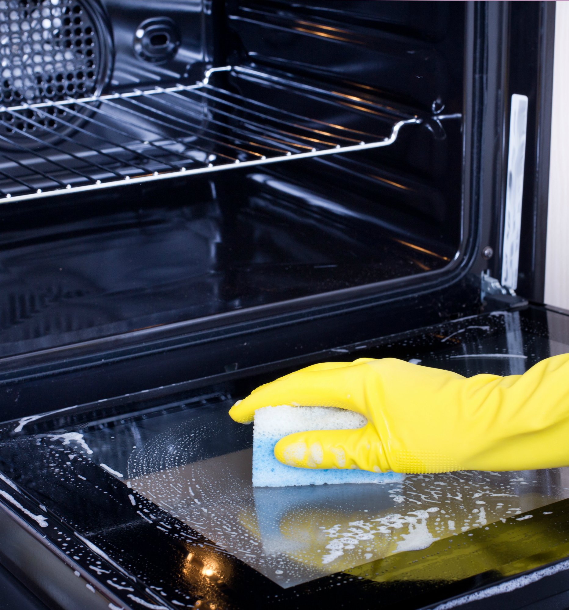 Close up of female hand with yellow protective gloves cleaning oven door