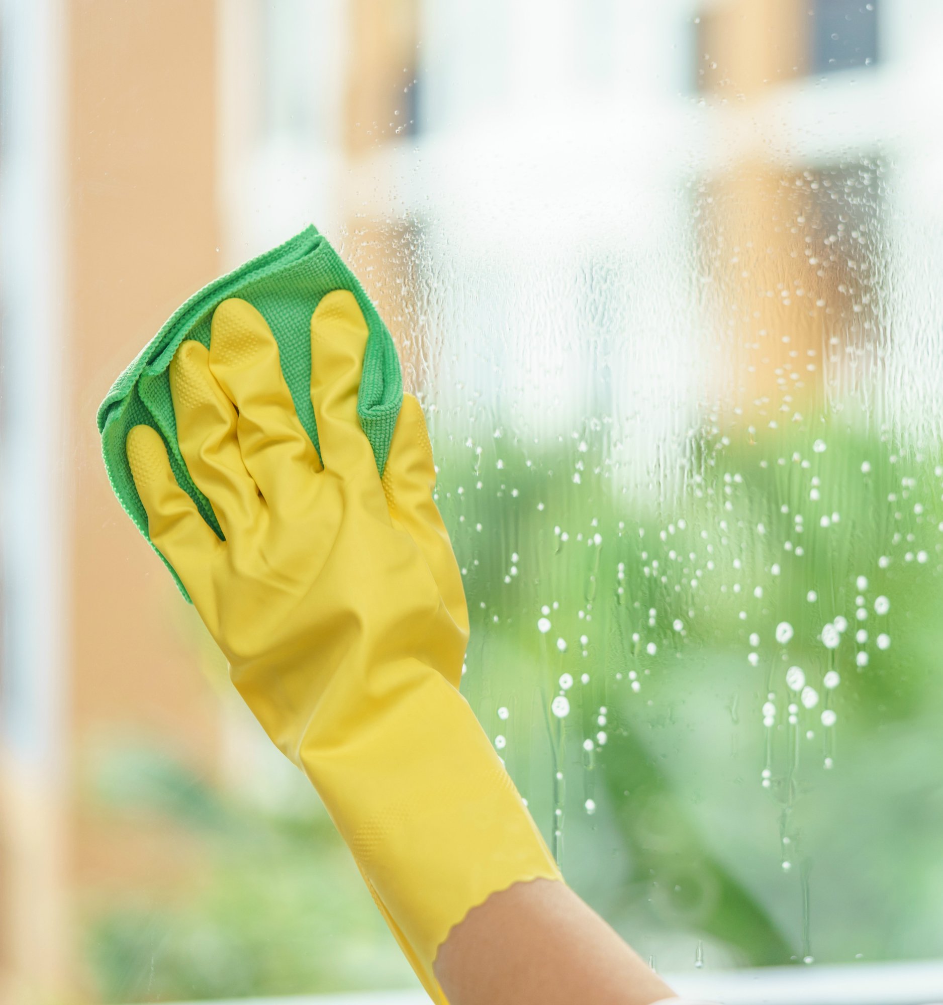 Woman housekeeper cleaning the mirror with green cloth.