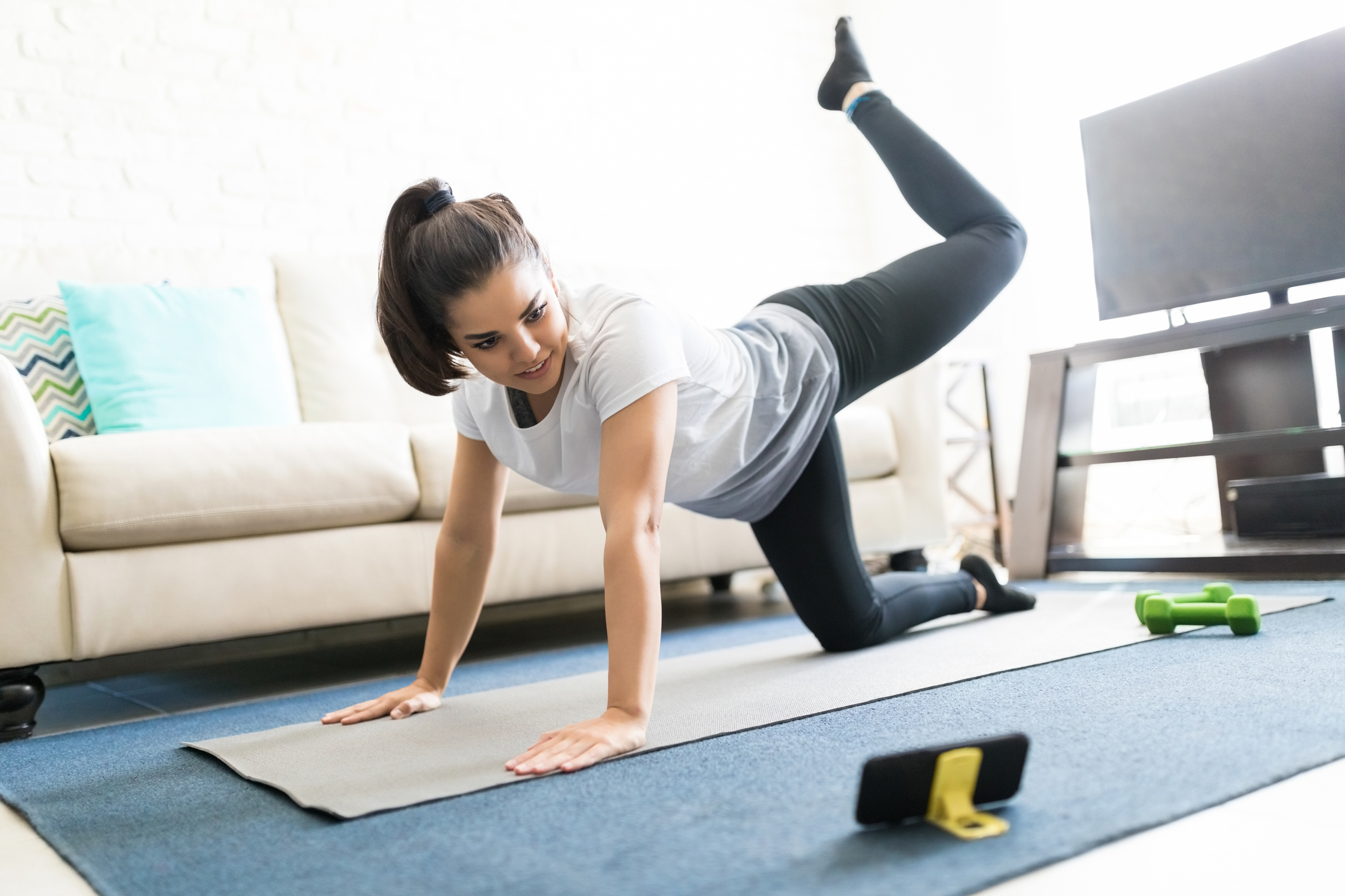 Woman doing exercises through online videos - Beautiful latin young woman repeating exercises while watching online exercise session on her smart phone at home