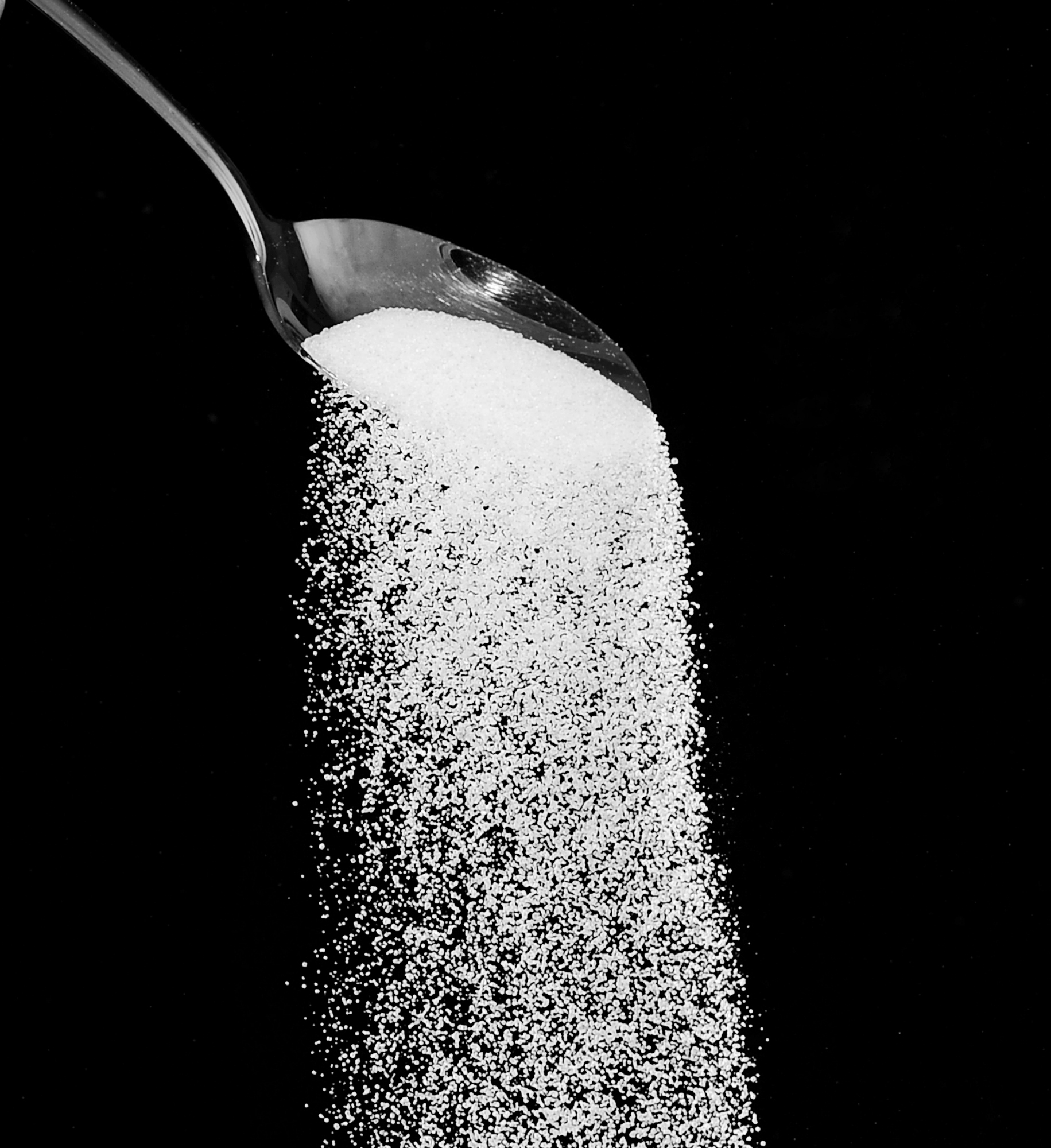 Sugar being poured from spoon with a dark background