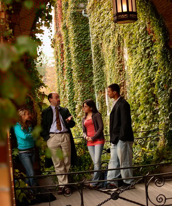 A literature professor stands outside with a group of students to discuss about a class project.