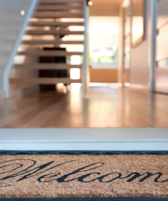 Close up of a welcome mat in front of an inviting house