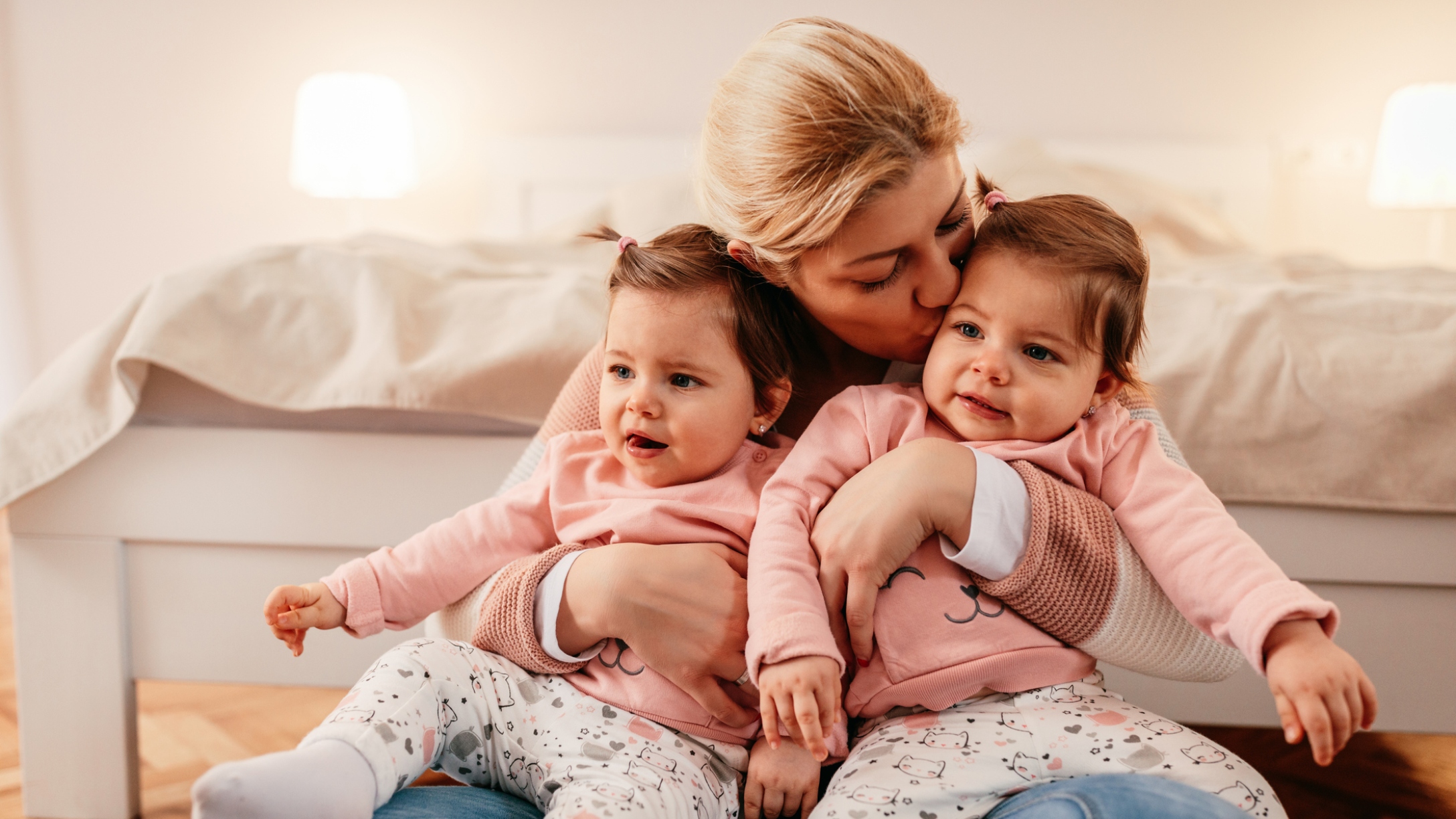 Mom holds twin baby girls and kisses one of them