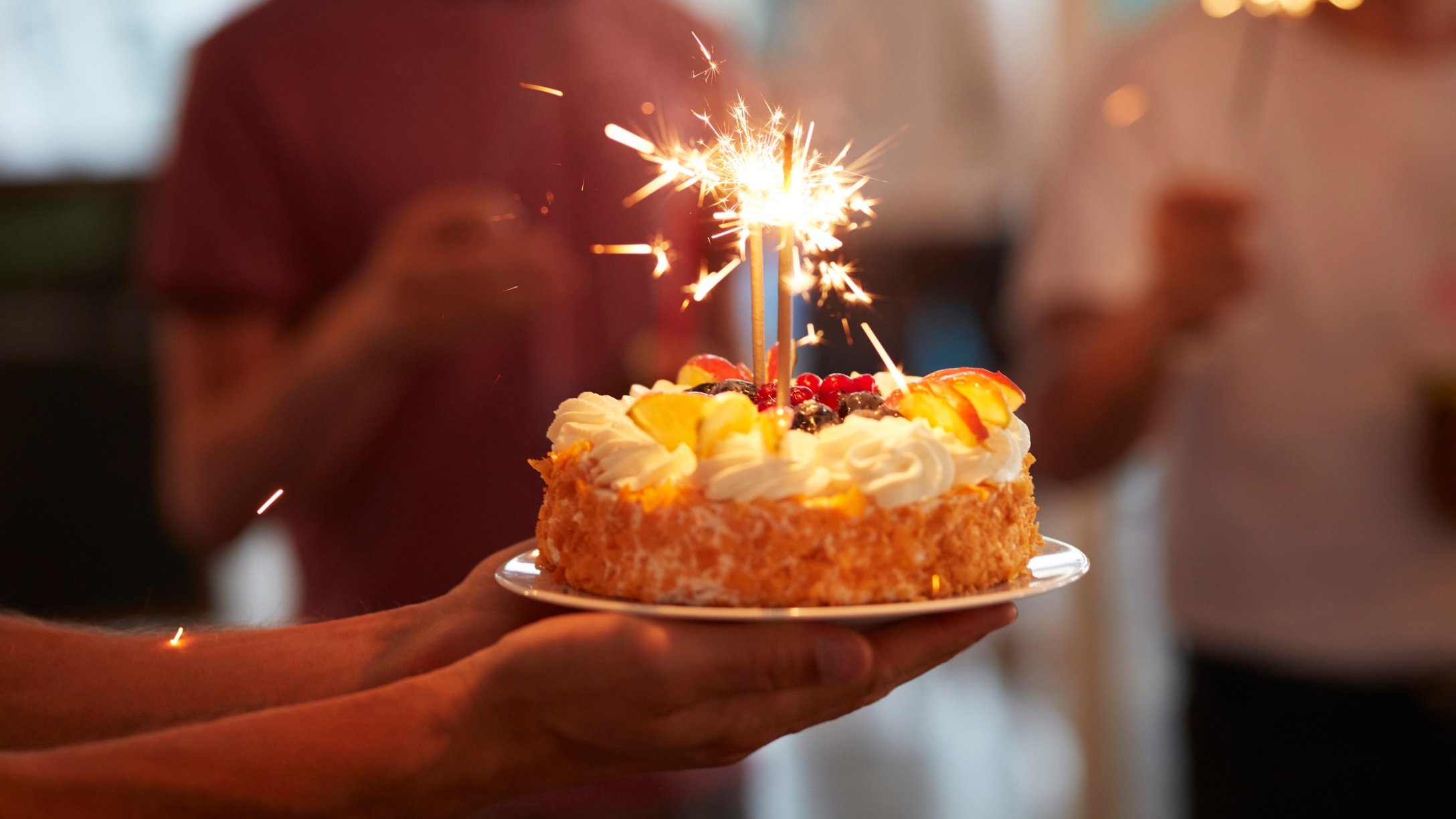 People gather round birthday cake with candles lit