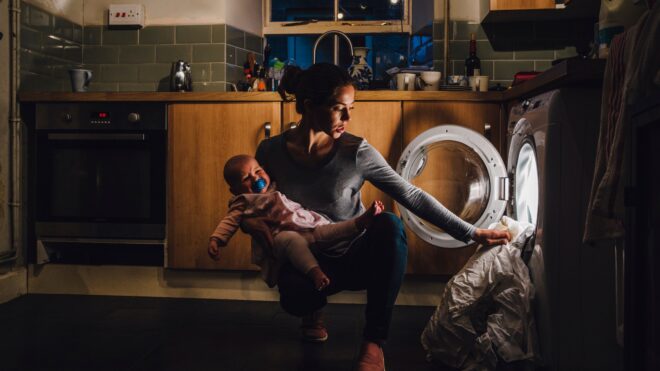Tired mom holds baby while doing the laundry