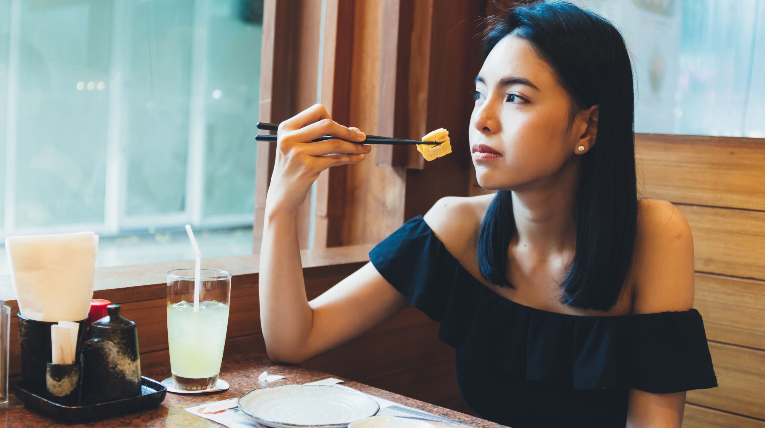 Attractive Asian woman sitting and eating Japanese food alone in the restaurant.