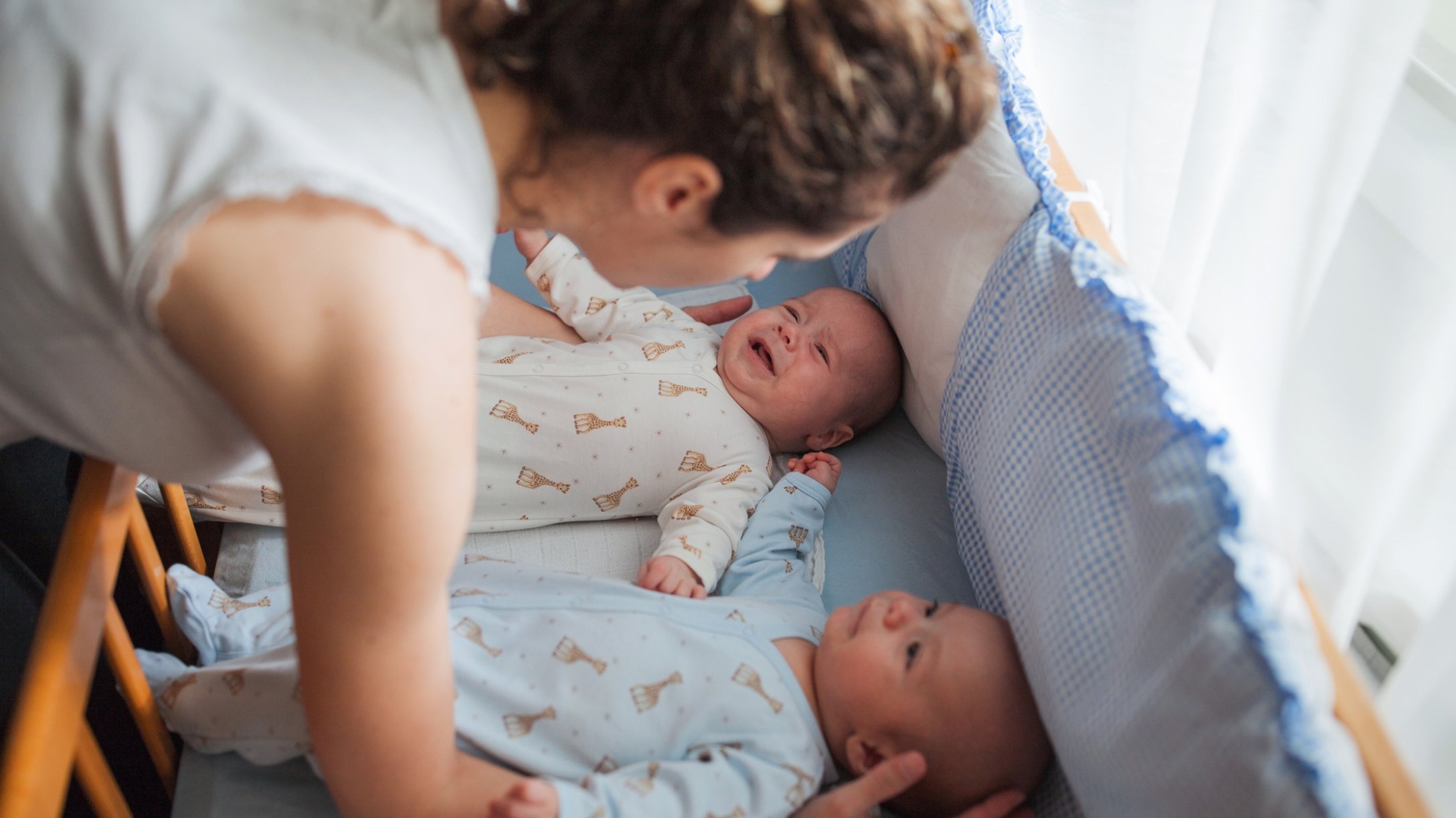 Mom tends to twin babies in crib
