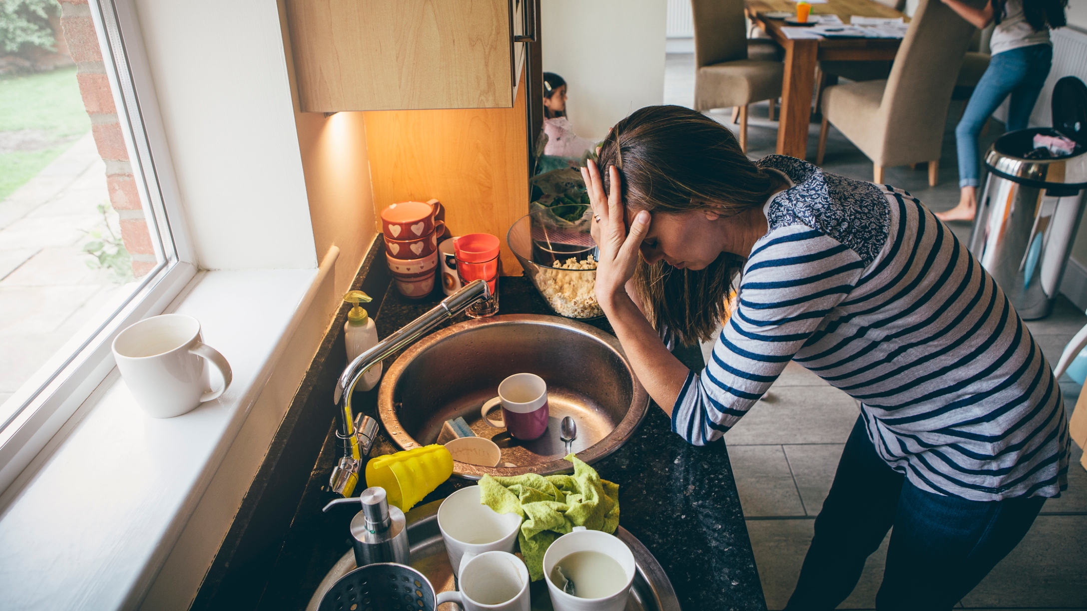 Stressed-out mom stands over sink full of dishes