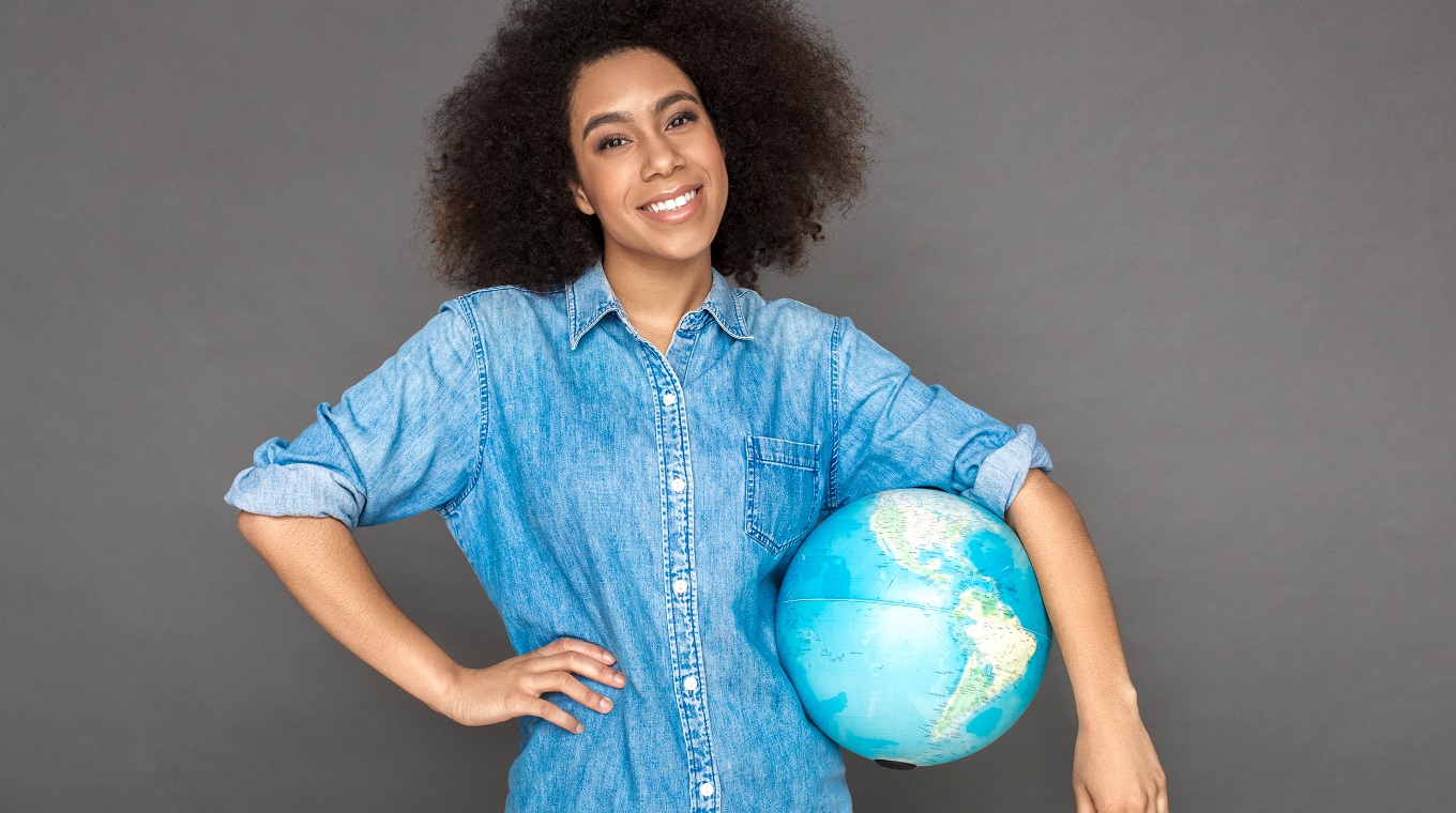 Freestyle. Mulatto woman standing isolated on grey with terrestrial globe smiling happy