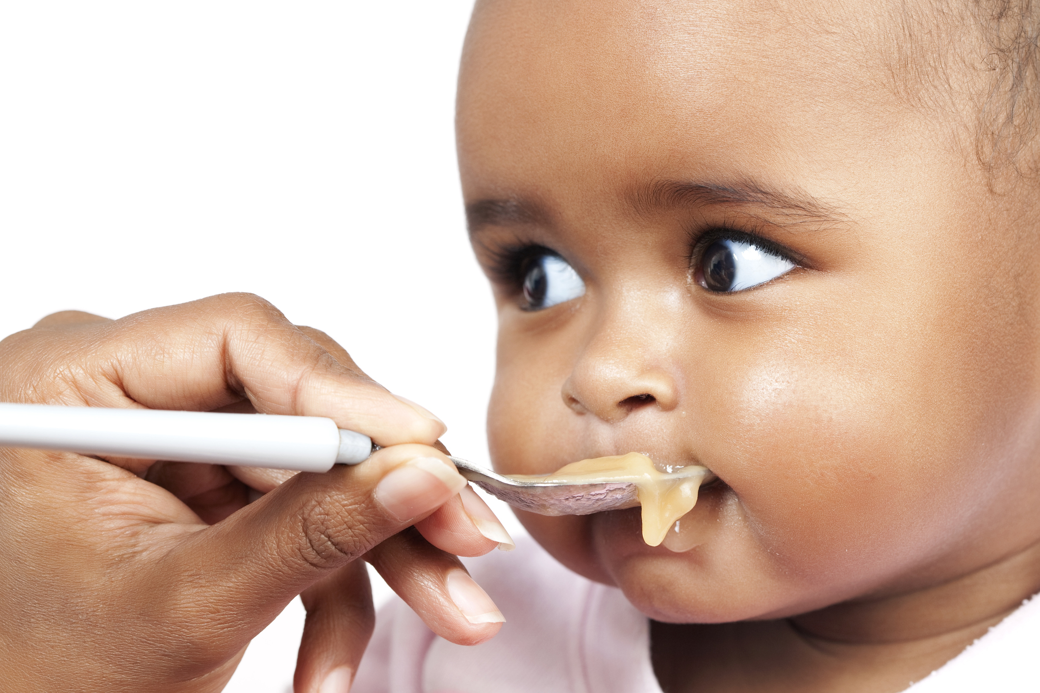 A baby being fed baby food on a white spoon