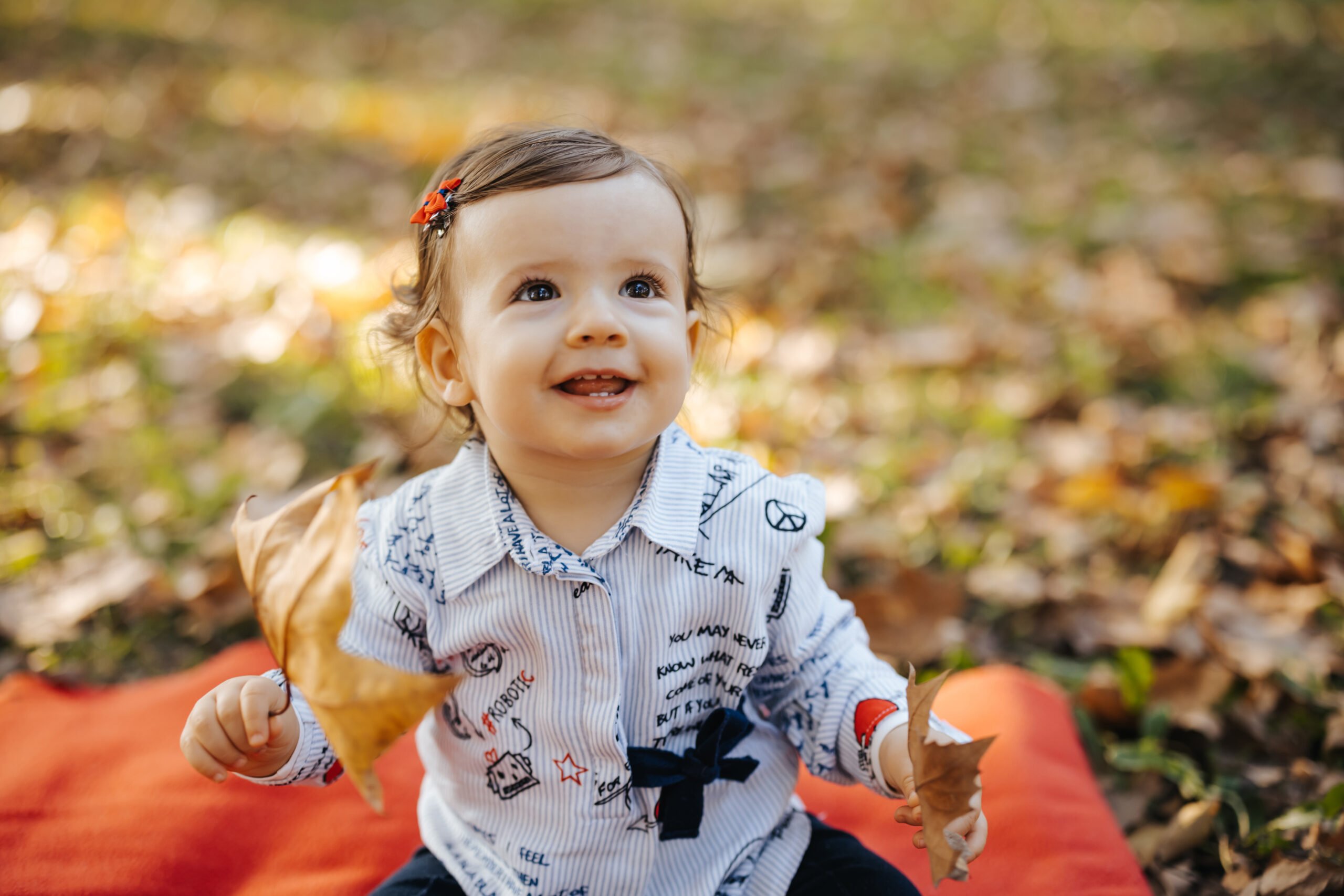 Cute one year old girl is sitting on picnic blanket in autumn park