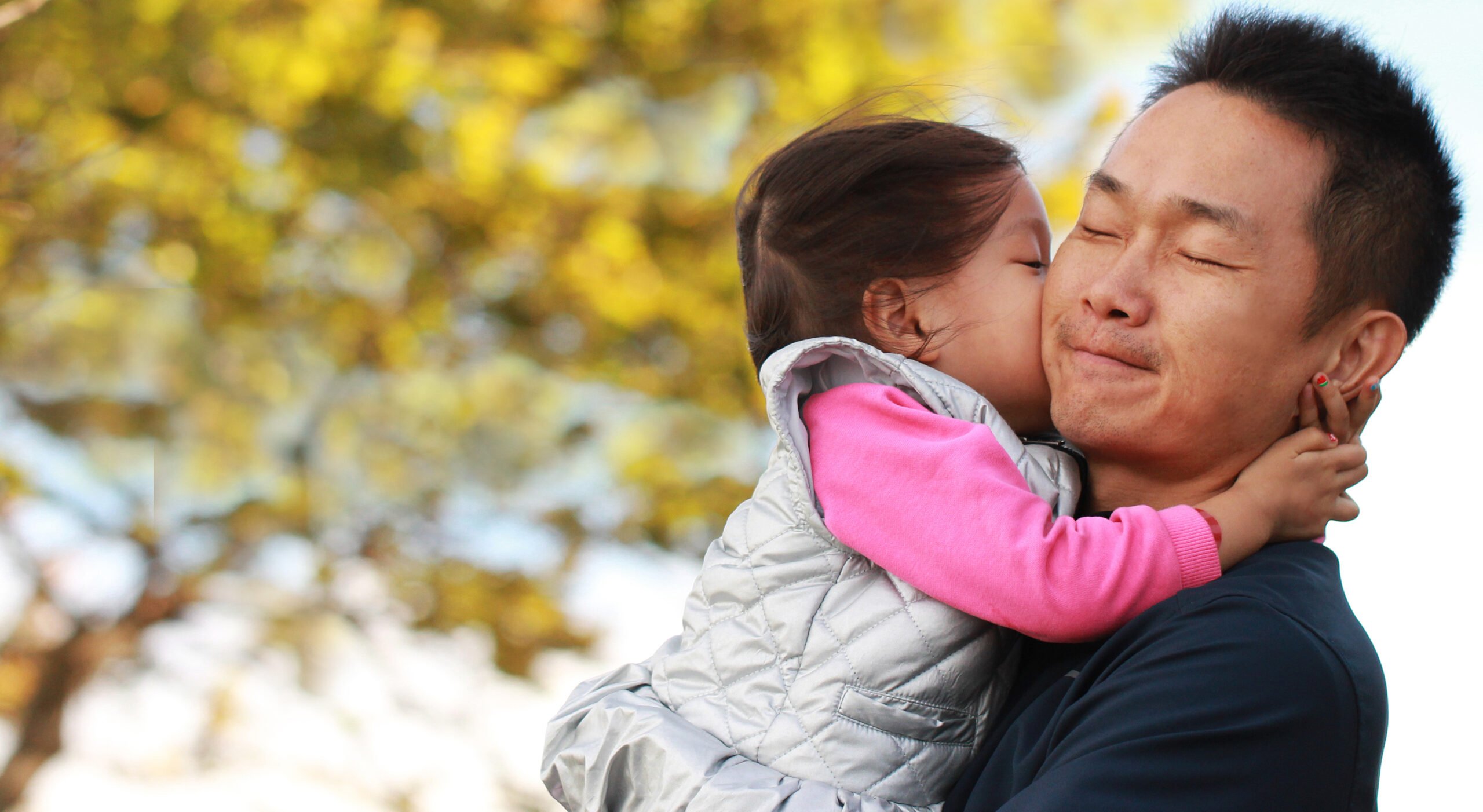 a daughter kissing his father in a park.