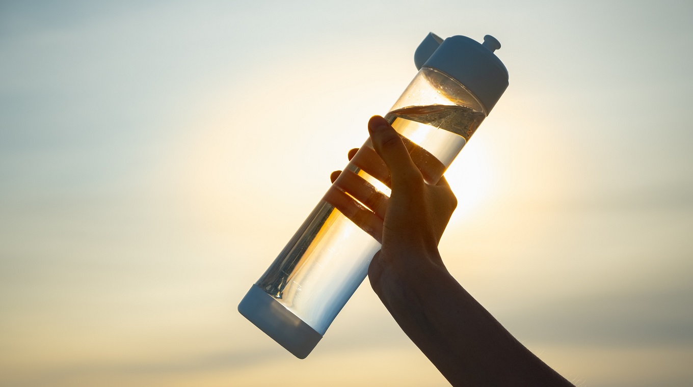 Human hand holds a water bottle against the setting sun.