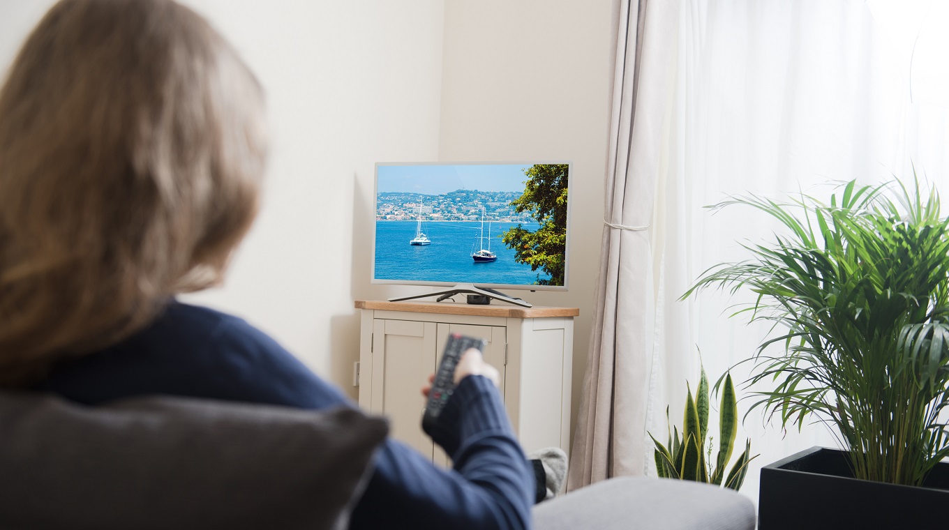 Woman sitting on sofa with remote control in her hand, while watching television in the domestic living room at home