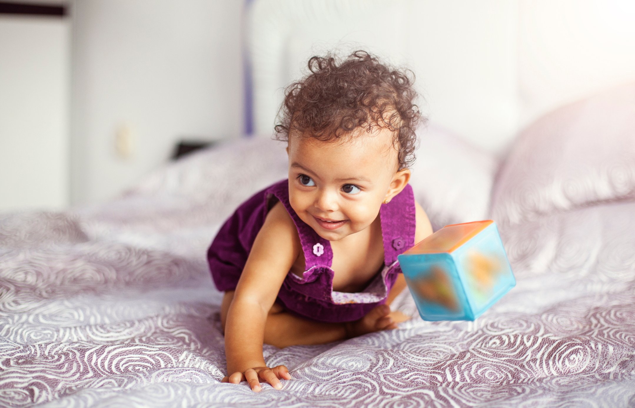 Cute baby girl playing with cube toy on bed