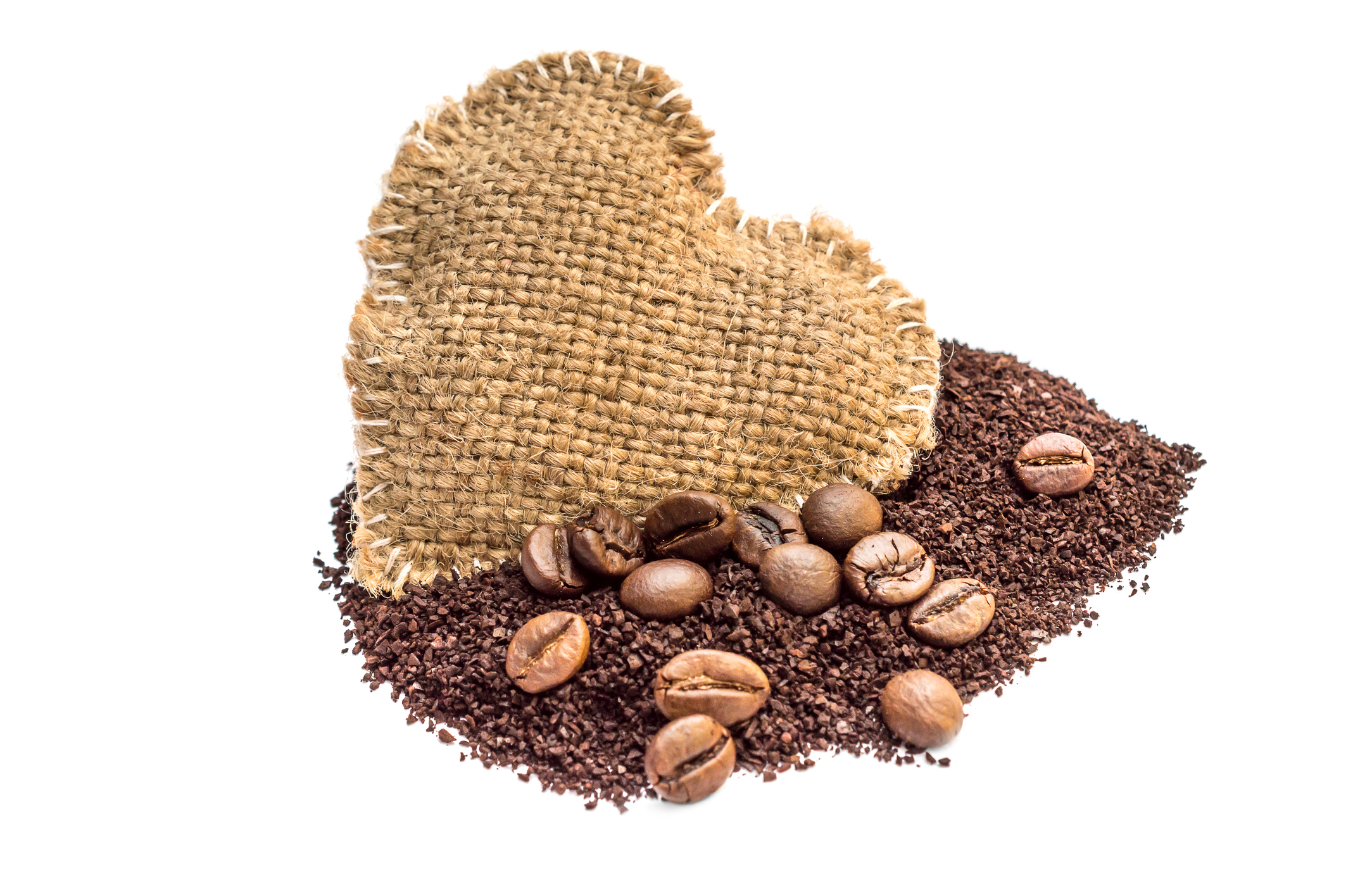 Heap of ground coffee with coffee beans and heart of burlap on white.