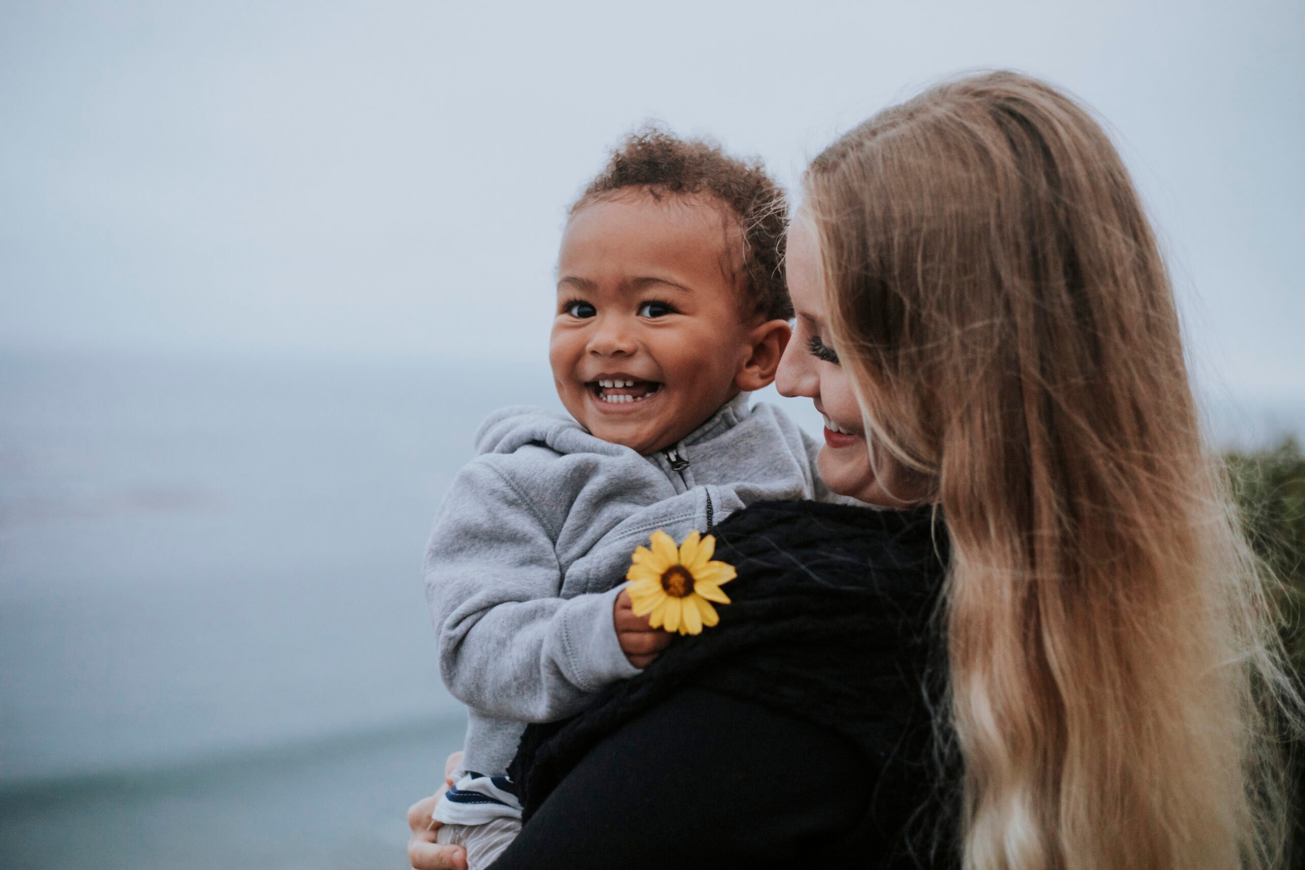 Young boy holding a flower carried by his mom