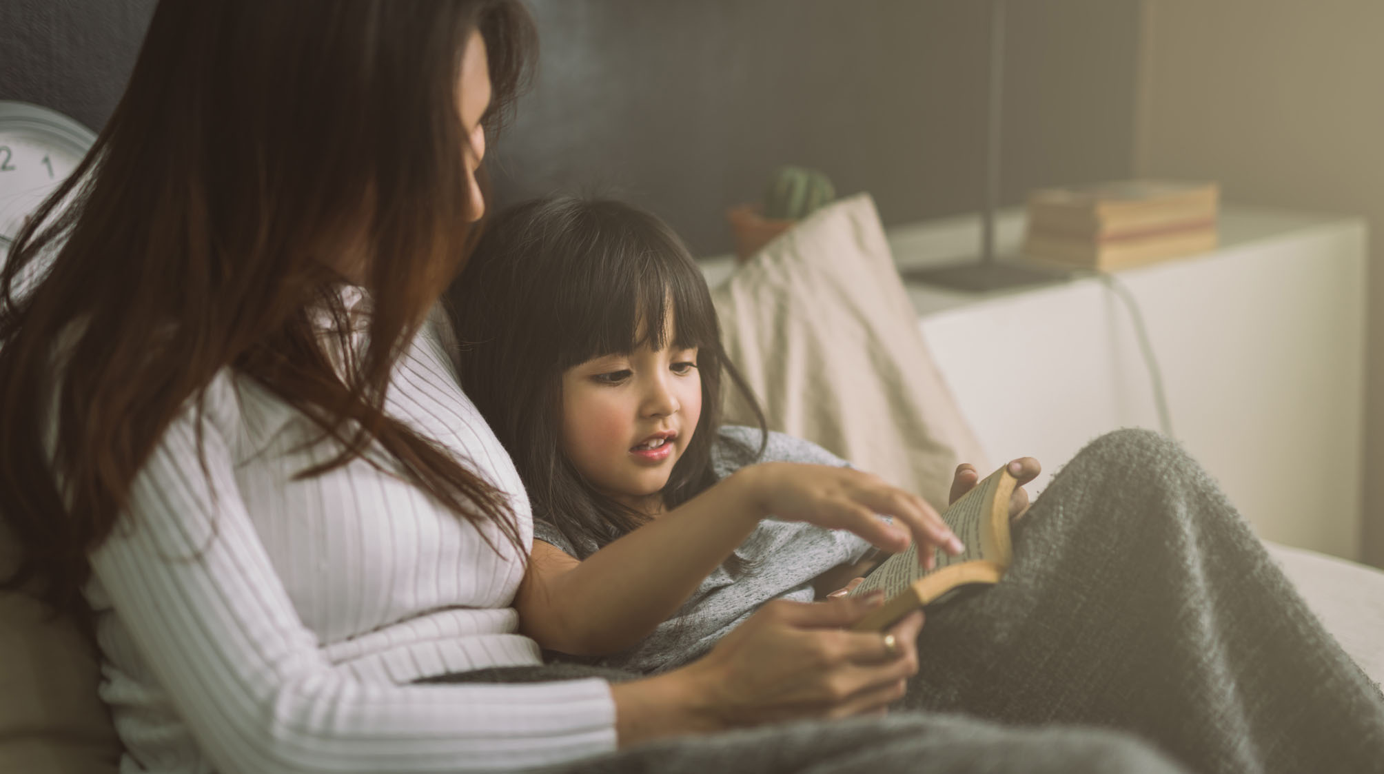 mother and daughter reading book at home in the bedroom